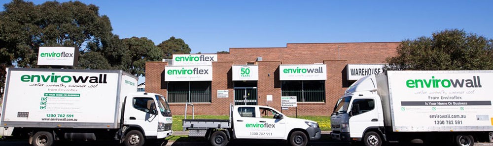 Fleet of Enviroflex vehicles parked outside a brick warehouse with Enviroflex and Envirowall signage on the building and trucks.