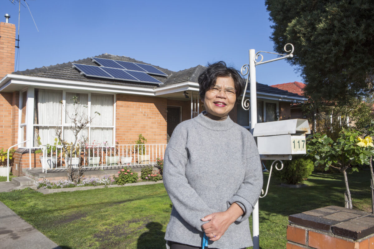 Woman standing in front of her house with solar panels on the roof.
