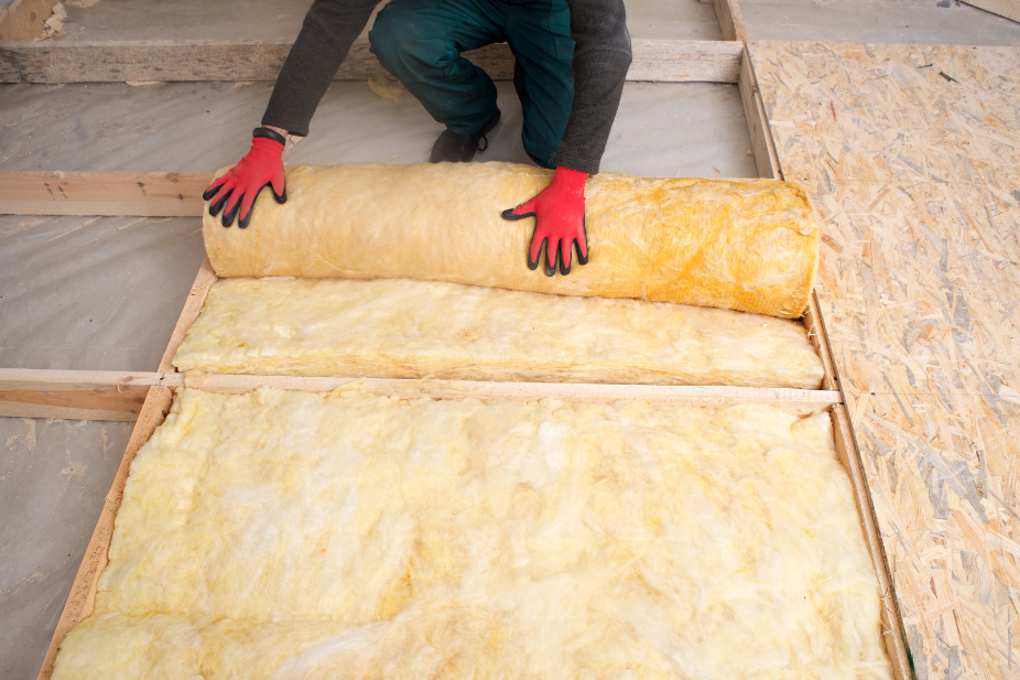 Image of a person wearing gloves installing insulation batts in a floor.