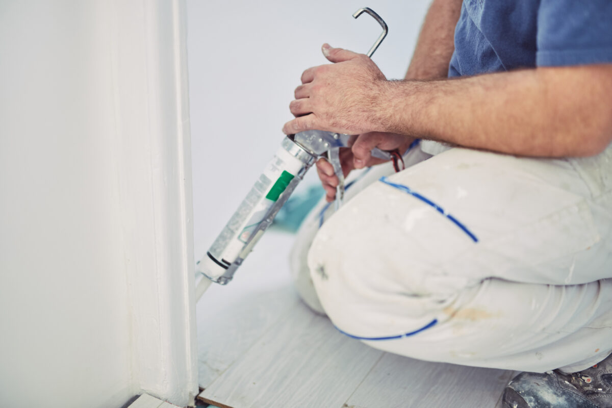 Close-up of a person sealing a gap along the edge of a door frame using a caulking gun to draught-proof the room.
